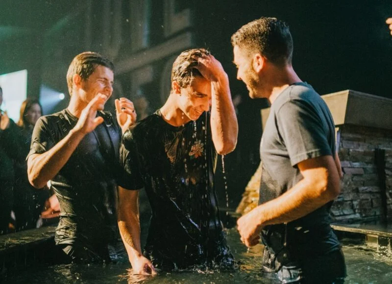 A man being baptized in the water with friends celebrating around him